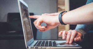 sideview of a laptop with two person's hand pointing to laptop's screen